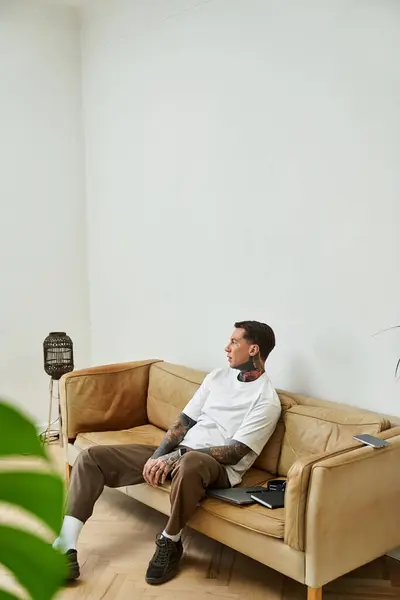 A young man sits pensively on his sofa at home, enjoying a quiet moment in a chic, minimalist space. — Stock Photo