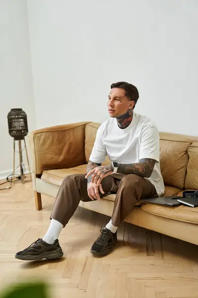 A stylish young man sits comfortably on a couch, lost in thought about life moments. — Stock Photo