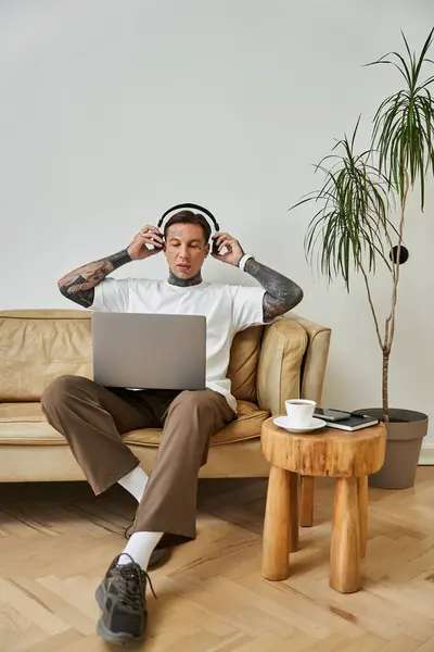 The young man enjoys music at home, immersed in his laptop while seated comfortably. — Stock Photo