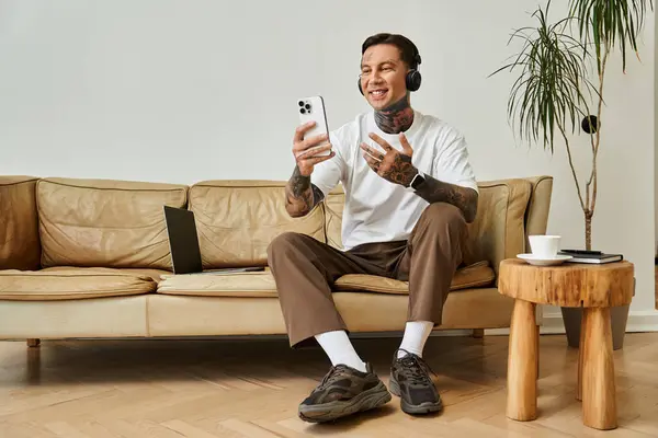 A stylish young man lounges at home, engaged in a cheerful video call with laughter. — Stock Photo