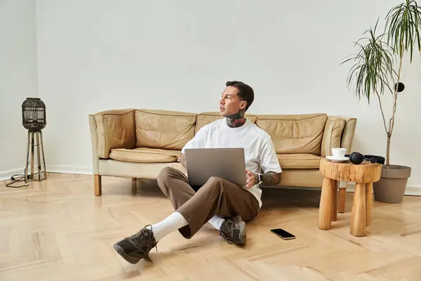 The young man sits on the floor, focused on his laptop, surrounded by a tranquil home environment. — Stock Photo