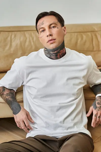 A stylish young man with tattoos enjoys a relaxed moment on a cozy couch at home. — Stock Photo
