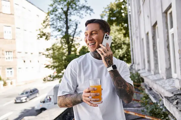 A happy young man enjoys a drink outdoors, chatting on the phone in the sunlight. — Stock Photo