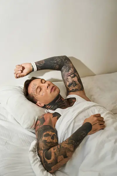 A young man with tattoos rests peacefully at home, enjoying a tranquil moment in bed. — Stock Photo