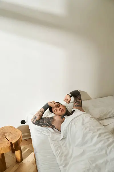 A relaxed young man lounges in bed, soaking in sunlight and enjoying a tranquil morning. — Stock Photo