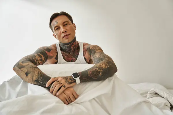 A young man with striking tattoos sits comfortably in bed, exuding relaxed confidence and style. — Stock Photo