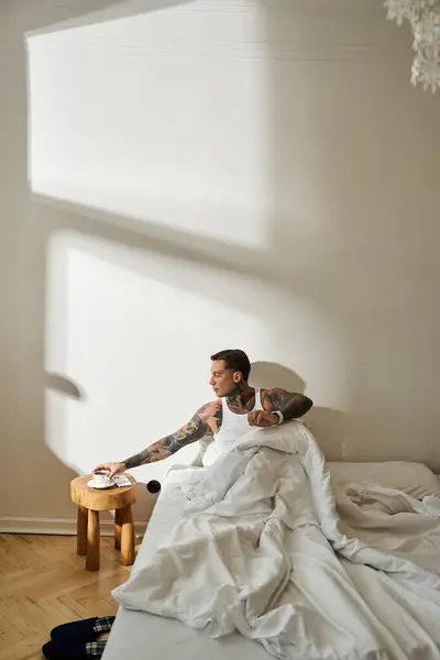A young man with tattoos stretches in bed, reaching for a plate on a bedside table. — Stock Photo