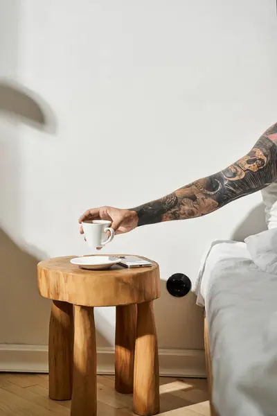 Un jeune homme à la maison prenant son café tout en se relaxant au lit près d'une table en bois unique. — Photo de stock