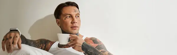 A young, tattooed man relaxes at home, savoring a warm cup of coffee in thoughtful reflection. — Stock Photo