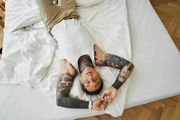 A young man lounges comfortably on a bed, embracing tranquility in a bright room. — Stock Photo