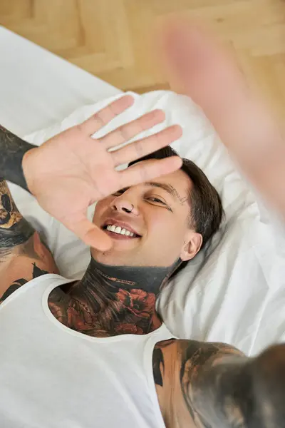 The man, with tattoos covering his arms, smiles joyfully in a relaxed atmosphere at home. — Stock Photo