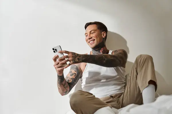 Ein stilvoller junger Mann entspannt sich zu Hause und lächelt freundlich, während er mit seinem Smartphone interagiert. — Stockfoto