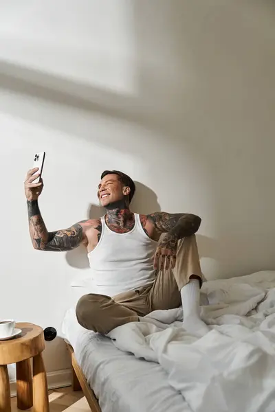 A young, handsome man enjoys a cheerful moment at home, sitting on his bed and taking a selfie. — Stock Photo