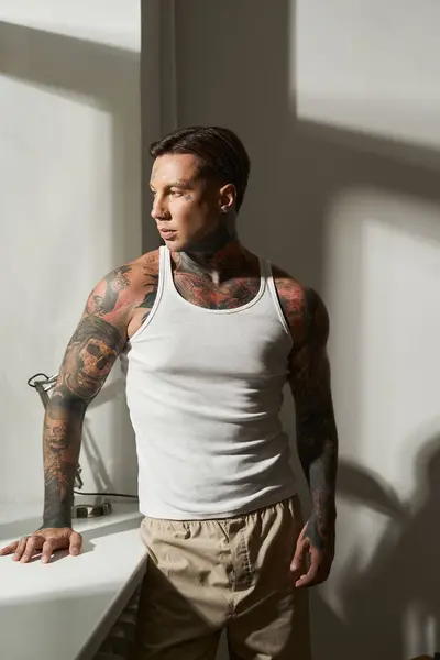Ein junger Mann mit Tätowierungen lehnt zu Hause an einem Tresen und genießt das weiche Licht. — Stockfoto