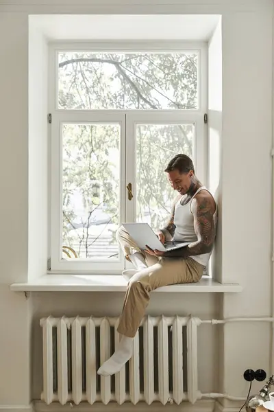 Inside a bright, warm home, a young man engages in work while sitting on a windowsill. — Stock Photo