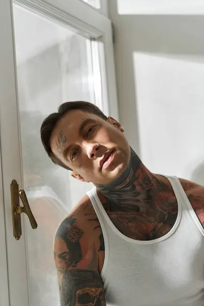 A young man relaxes at home, bathed in soft afternoon light that showcases his tattoos. — Stock Photo
