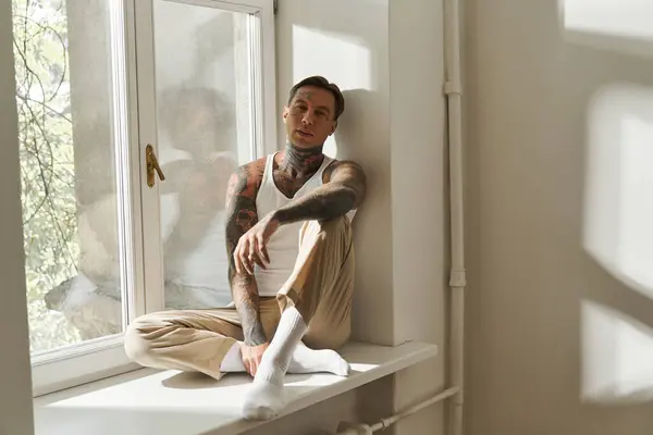El joven se sienta tranquilamente en un alféizar de la ventana, disfrutando de la cálida luz del sol que entra. — Stock Photo