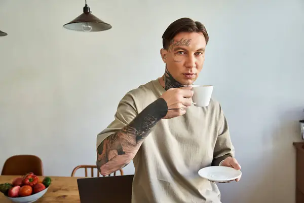 Красивый молодой человек, потягивающий кофе, стоя на своей стильной кухне, выглядящий заботливо. — стоковое фото