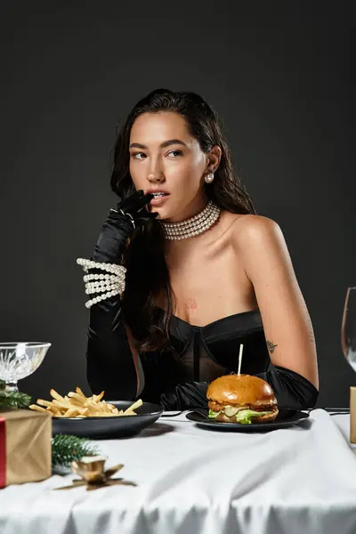 A glamorous woman indulges in a gourmet burger while wearing elegant gloves and pearls. — Stock Photo