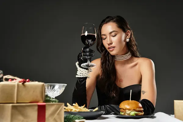 An elegantly dressed young woman raises a glass of red wine, enjoying a luxurious dining experience. — Stock Photo