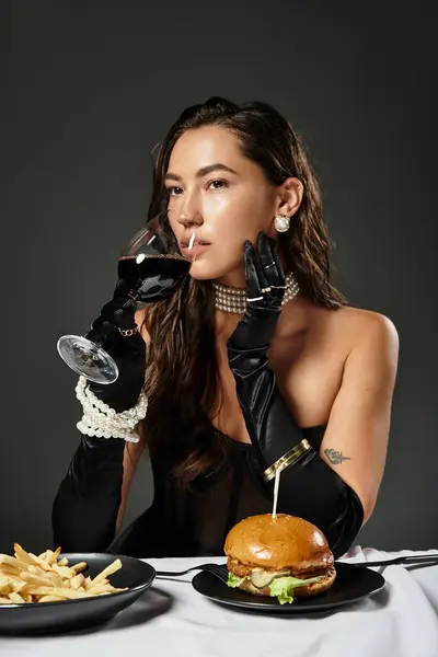 A young woman in elegant attire savors wine while seated at an exquisite table with food. — Stock Photo