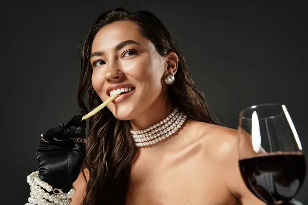 A young woman dressed elegantly holds a glass of red wine while playfully enjoying a snack. — Stock Photo