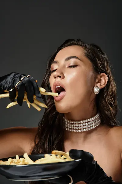 Una donna elegante gode di patatine fritte gourmet, vestita con stile e raffinatezza radiante. — Foto stock