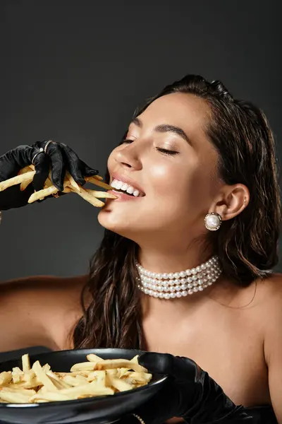 Une belle dame en robe luxueuse goûte les frites gourmandes avec joie et élégance. — Photo de stock