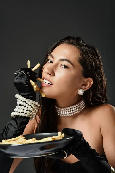 Uma mulher glamourosa gosta de batatas fritas, mostrando sofisticação no elegante desgaste da noite. — Fotografia de Stock