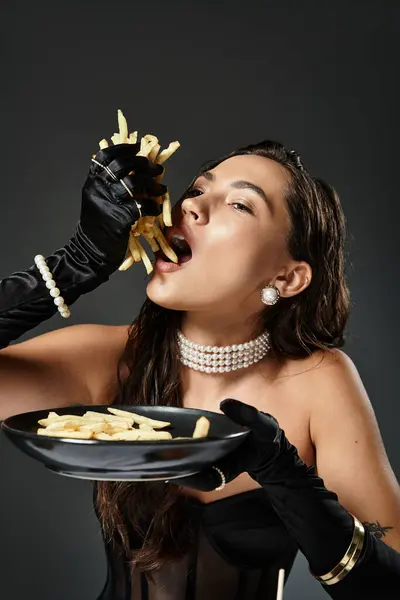 Une jeune femme en tenue élégante aime les frites gourmandes avec une élégance ludique. — Photo de stock