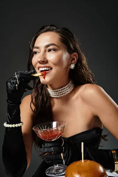 A mulher elegante, adornada em trajes deslumbrantes, saboreia um coquetel enquanto se delicia com um lanche. — Fotografia de Stock