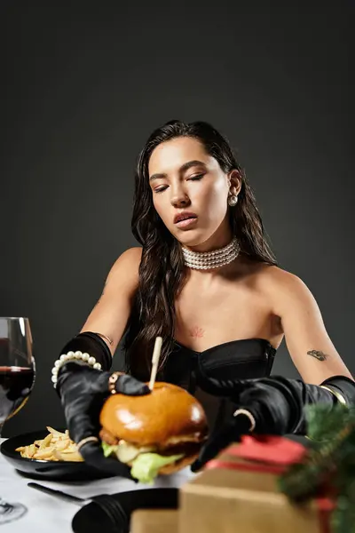 A sophisticated young woman dressed elegantly engages with a gourmet burger while dining. — Stock Photo