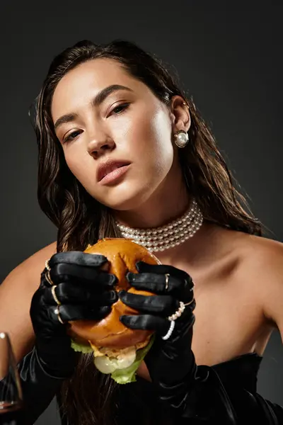 Eine junge, schöne Frau in eleganter Kleidung probiert einen Gourmet-Burger, der Raffinesse ausstrahlt. — Stockfoto