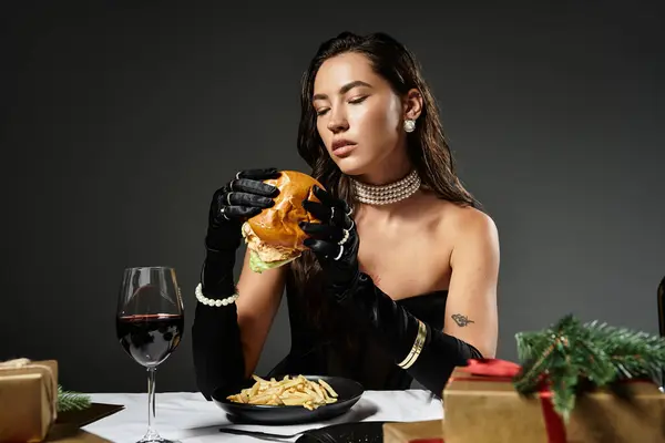 Une jeune femme en tenue élégante savoure un burger gastronomique aux frites et au vin, exsudant la sophistication. — Photo de stock