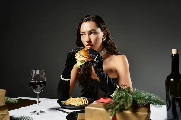 A young woman in elegant attire indulges in a gourmet burger and fries while seated. — Stock Photo