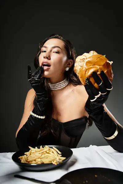 Eine elegant gekleidete junge Frau gönnt sich einen Gourmet-Burger und Pommes, während sie Zuversicht ausstrahlt. — Stockfoto