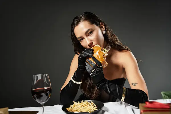 Uma jovem sofisticada saboreia um hambúrguer gourmet enquanto se veste elegantemente em uma mesa luxuosa. — Fotografia de Stock