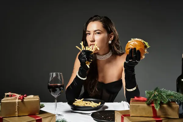 A young woman in elegant attire savors a burger and fries during a festive gathering. — Stock Photo
