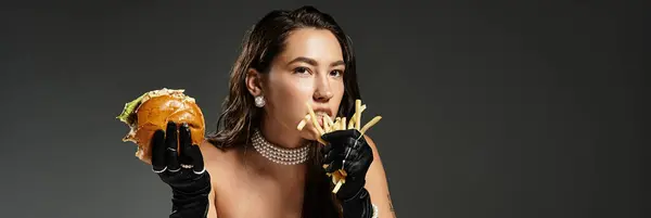 An elegant woman enjoys gourmet fries and a burger, showcasing her refined yet playful style. — Stock Photo
