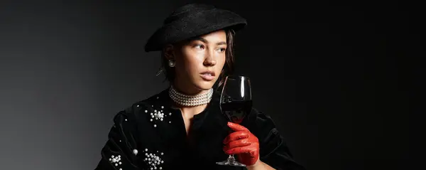 The sophisticated woman holds a glass of red wine, showcasing her elegant attire and style. — Stock Photo
