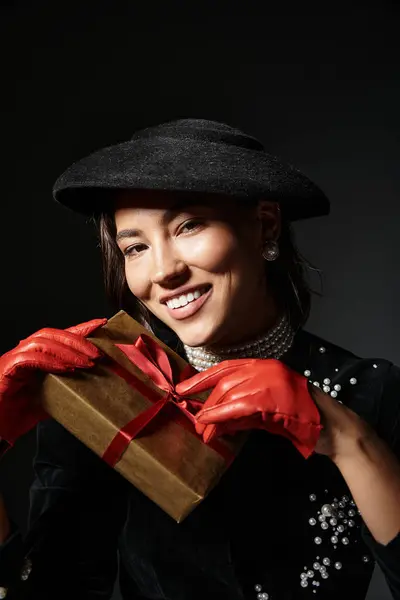 A stylish woman exudes charm while holding a gift adorned with a ribbon, dressed in elegant attire. — Stock Photo