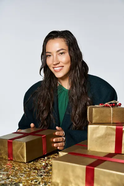 The sophisticated woman with long hair smiles warmly as she arranges beautifully wrapped presents. — Stock Photo