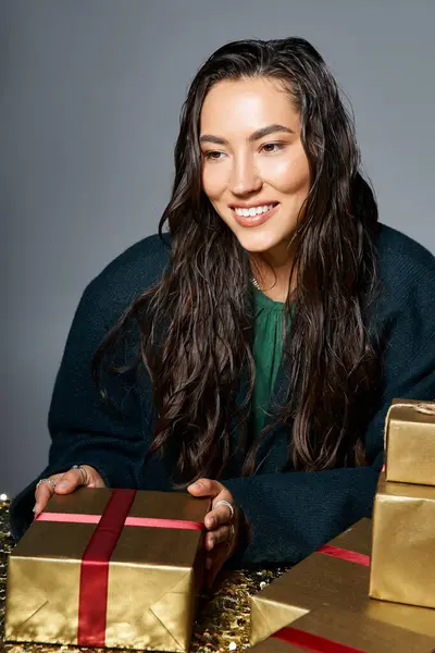 A sophisticated woman with wet hair smiles as she arranges golden presents for a special occasion. — Stock Photo