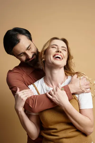 A man embraces a woman while she laughs joyfully in a cozy, soft toned setting. — Stock Photo