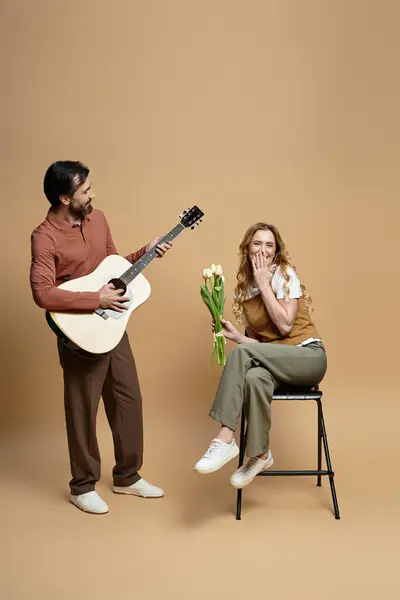 A joyful moment unfolds as a man plays guitar for a woman holding flowers in a cozy atmosphere. — Stock Photo