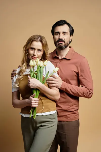 A middle aged couple shows affection, holding tulips against a warm colored background. — Stock Photo