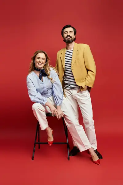 A middle aged couple showcases their unique fashion sense while smiling against a bold red backdrop. — Stock Photo