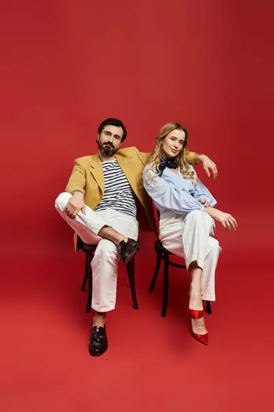 Una coppia di mezza età elegante posa con fiducia sulle sedie, irradiando fascino ed eleganza. — Foto stock