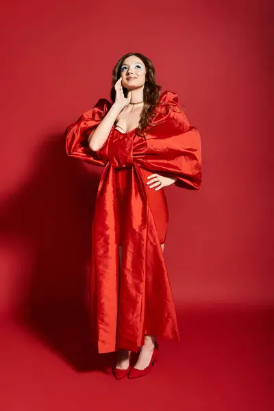 The young woman showcases a stunning red dress with dramatic sleeves while striking a playful pose. — Stock Photo