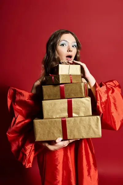 A delighted young woman showcases four elegant presents while dressed in stylish red attire. — Stock Photo